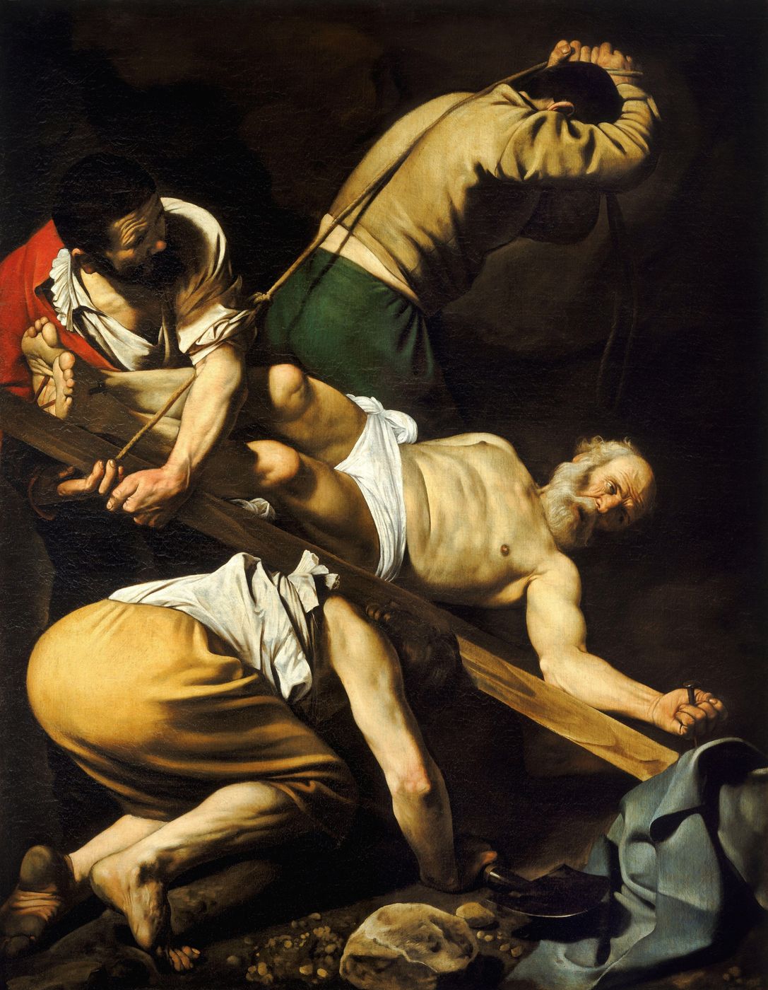 Petrus, ein alter Mann mit grauem Bart, ist an das schräg liegende Kreuz genagelt und blickt über die Schulter; drei Männer in einem dunklen Raum richten das Kreuz mit Seil und Körperkraft auf.